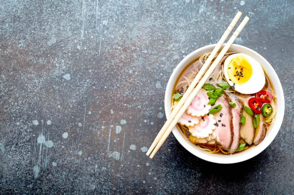 Japanese ramen bowl with egg, pork slices, and chopsticks.