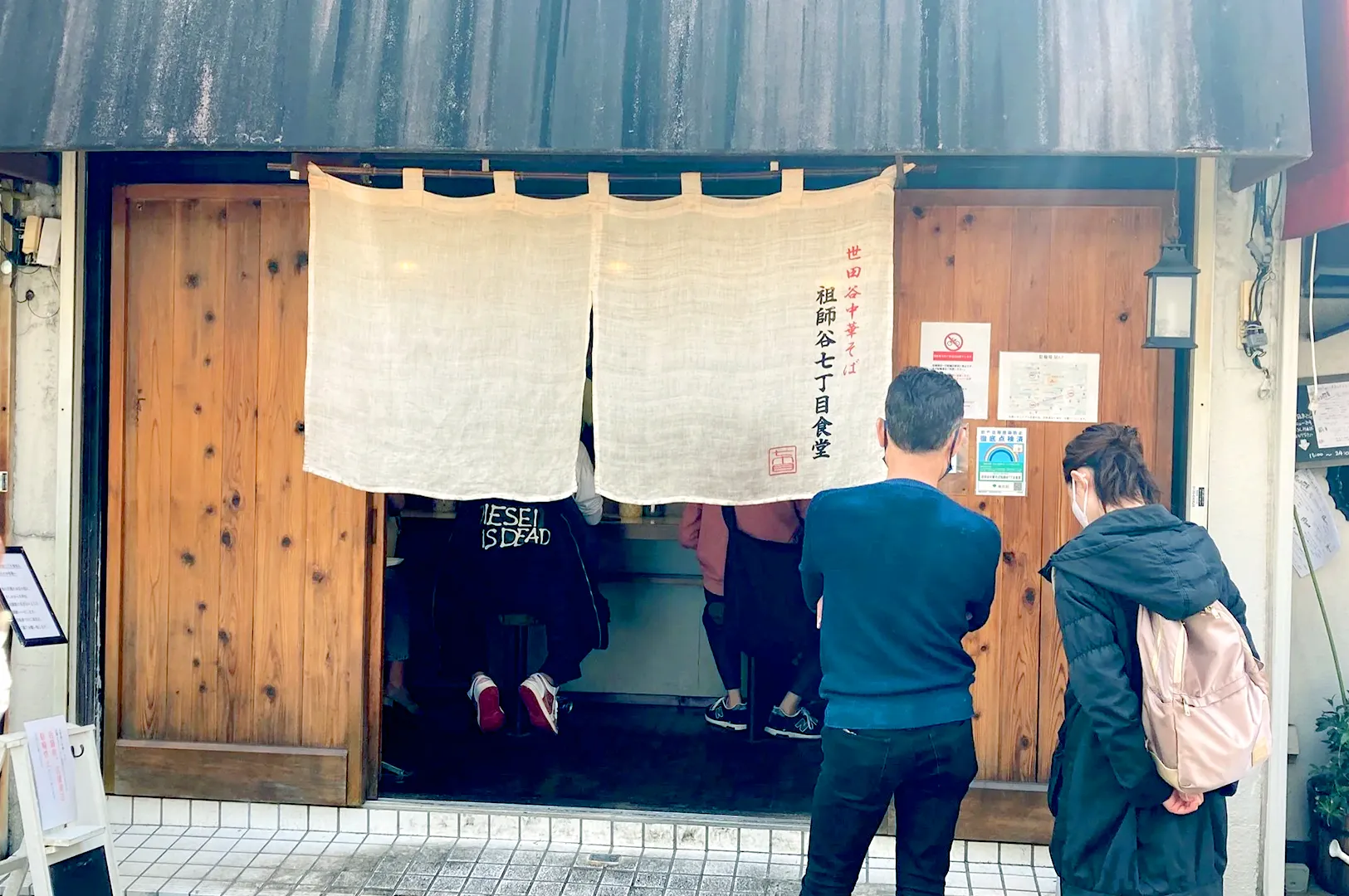 Small ramen shop with a noren curtain and customers waiting outside.