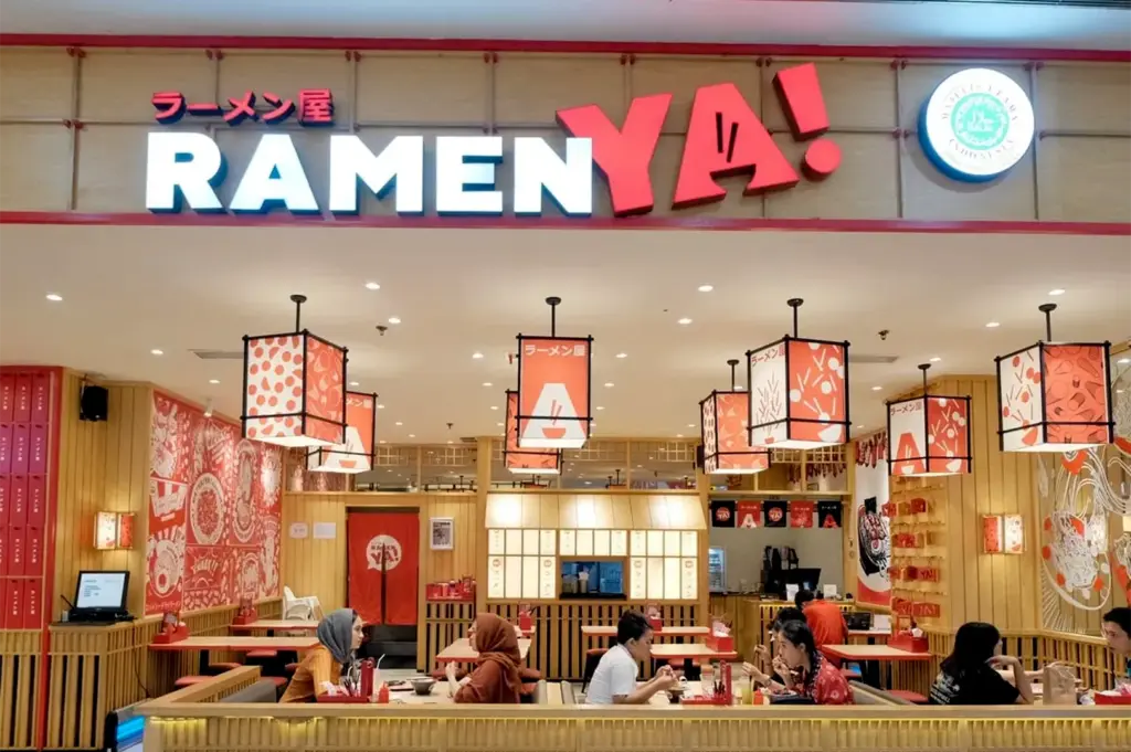 Interior view of a RamenYA! restaurant with customers dining, featuring Japanese-style wooden decor and modern hanging lanterns.