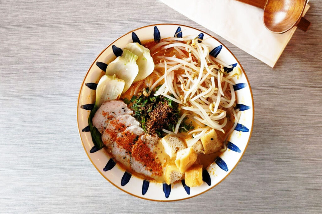Malaysian-style ramen with spicy broth, bean sprouts, tofu, and herbs in a fusion noodle bowl