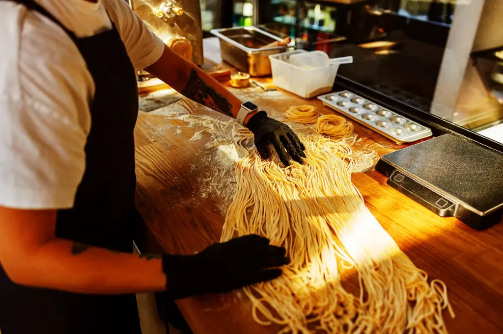 Chef preparing fresh ramen noodles on wooden counter with flour in a professional kitchen