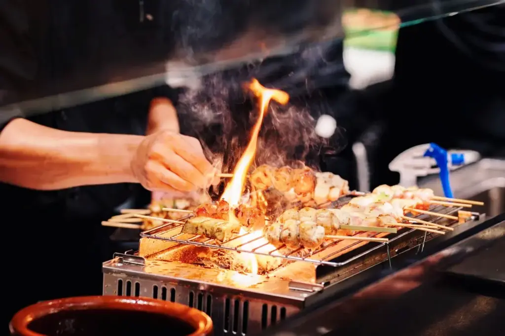 Yakitori skewers being grilled over charcoal fire in a Singapore izakaya kitchen