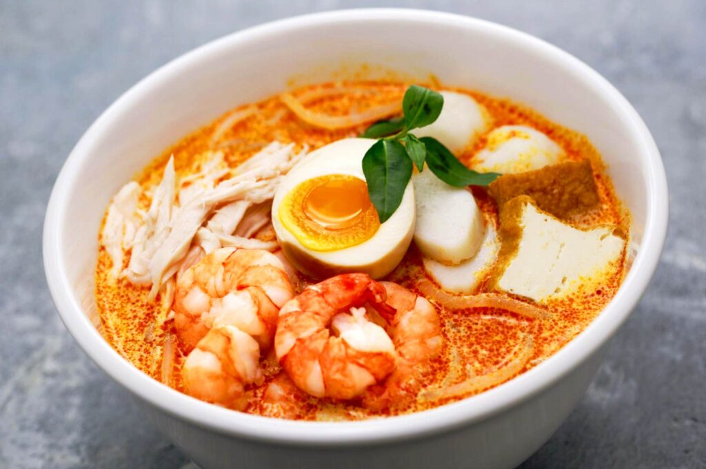 Singapore laksa ramen with prawns, soft-boiled egg, tofu and coconut spicy broth close-up