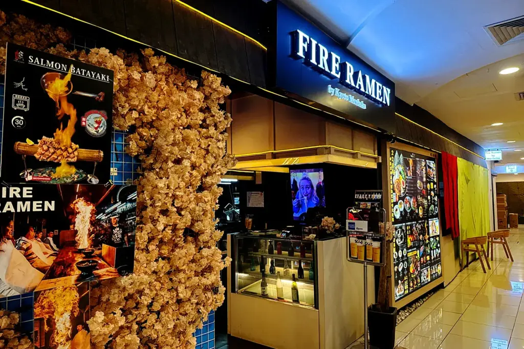 Fire Ramen by Menbaka Singapore storefront with illuminated signage, Japanese izakaya entrance and promotional flame ramen display in a modern mall setting
