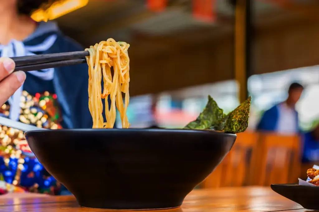 Chopsticks lifting noodles from ramen bowl