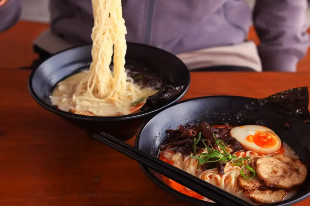 Two ramen bowls with lifted noodles