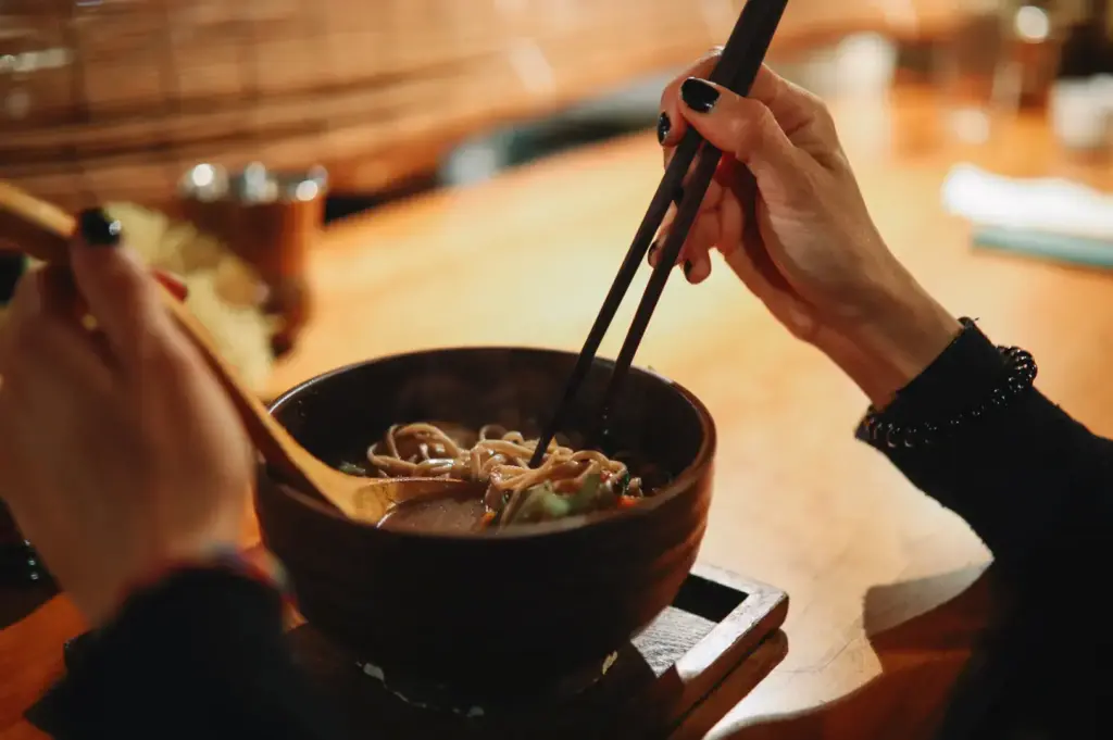 Hands with chopsticks over ramen bowl