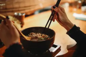 Hands with chopsticks over ramen bowl