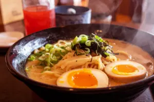 A steaming bowl of ramen with noodles, sliced eggs, and green onions.