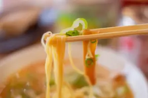 Close-up of ramen noodles being lifted with chopsticks, garnished with green onions and bamboo shoots.