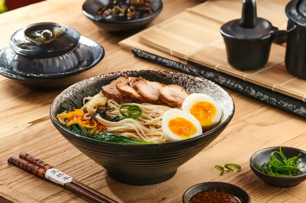 A bowl of Japanese ramen with sliced pork, soft-boiled eggs, and garnish on a wooden table.