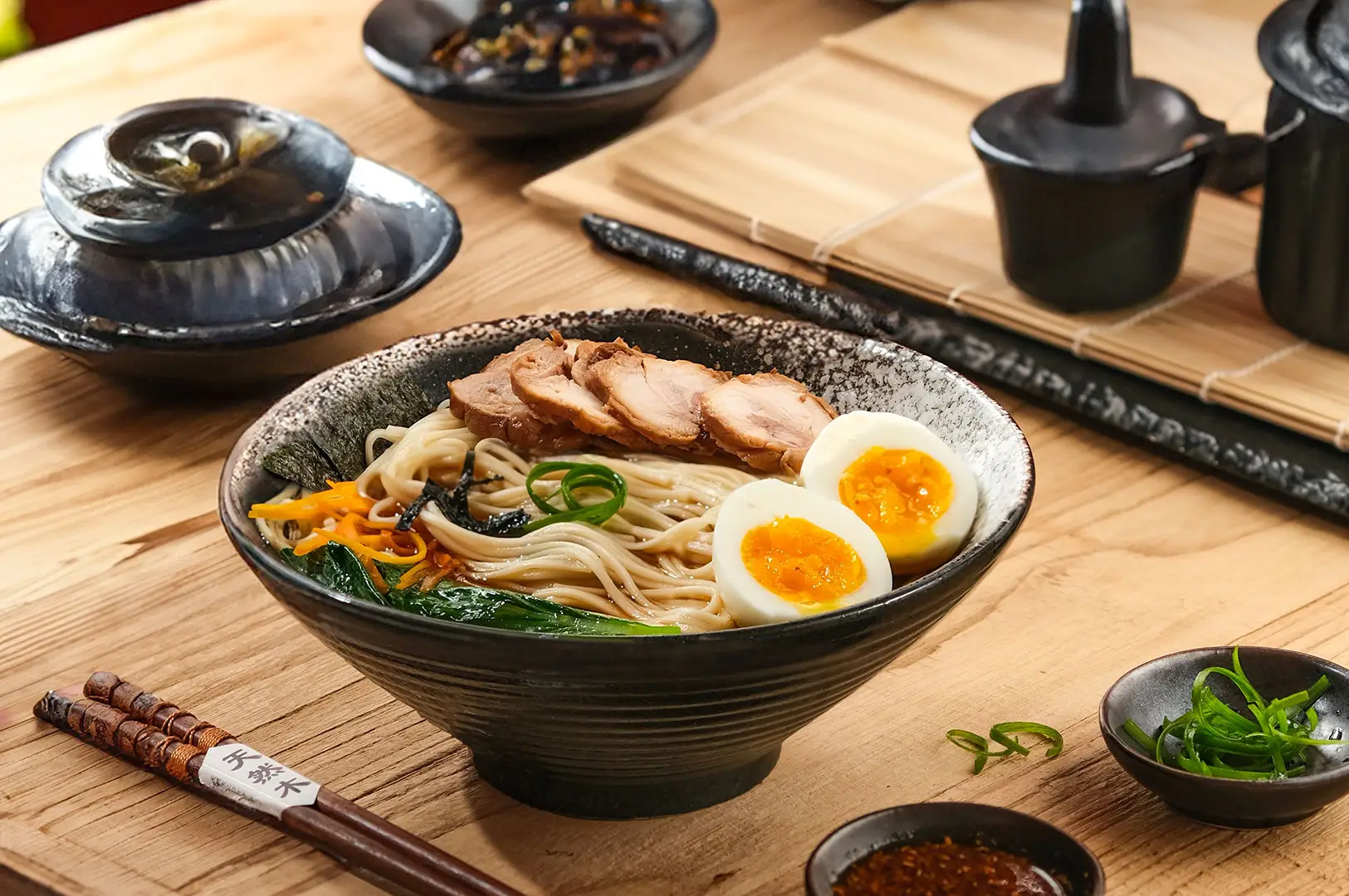 A bowl of Japanese ramen with sliced pork, soft-boiled eggs, and garnish on a wooden table.