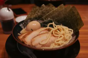 A bowl of tonkotsu ramen with sliced pork, noodles, a soft-boiled egg, and nori on a wooden table.