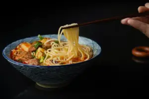 Close-up of ramen bowl with soft-boiled egg, chashu pork slices, scallions, sesame seeds, and thin noodles in clear broth.