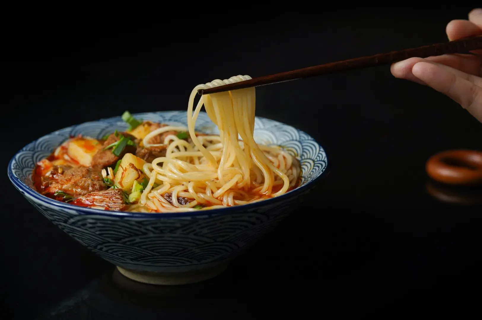 Close-up of ramen bowl with soft-boiled egg, chashu pork slices, scallions, sesame seeds, and thin noodles in clear broth.