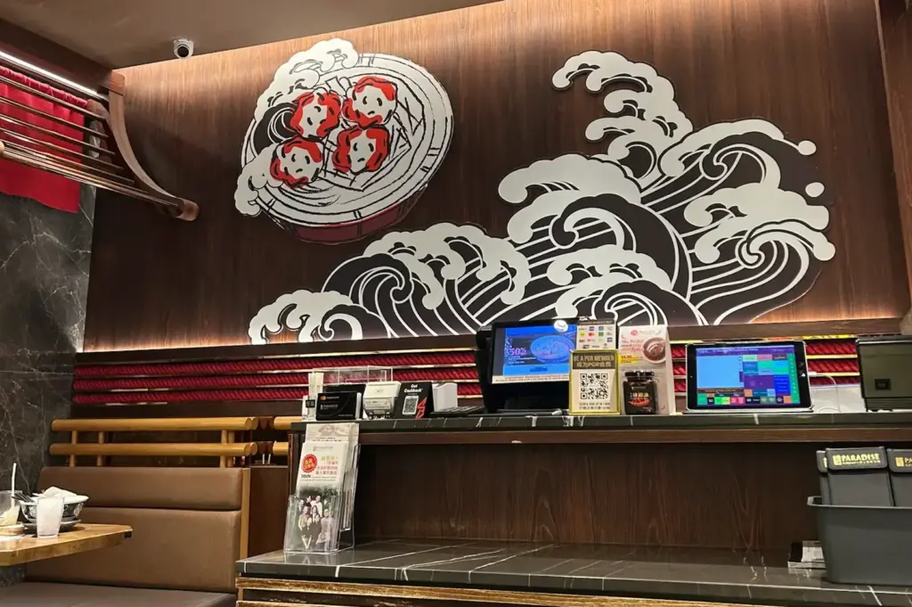 Le Shrimp Ramen counter with wave artwork, digital ordering screens, a QR code, and wooden seating.