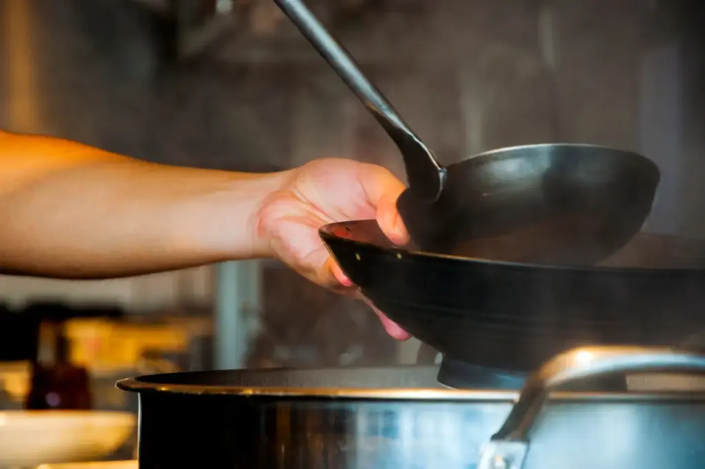 Hand pouring hot broth from a ladle into a ramen bowl over a pot.