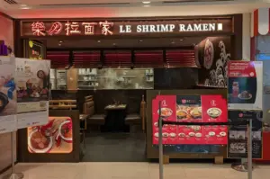 Le Shrimp Ramen storefront at Plaza Singapura with illuminated Chinese and English signage, menu boards, and a dining area.