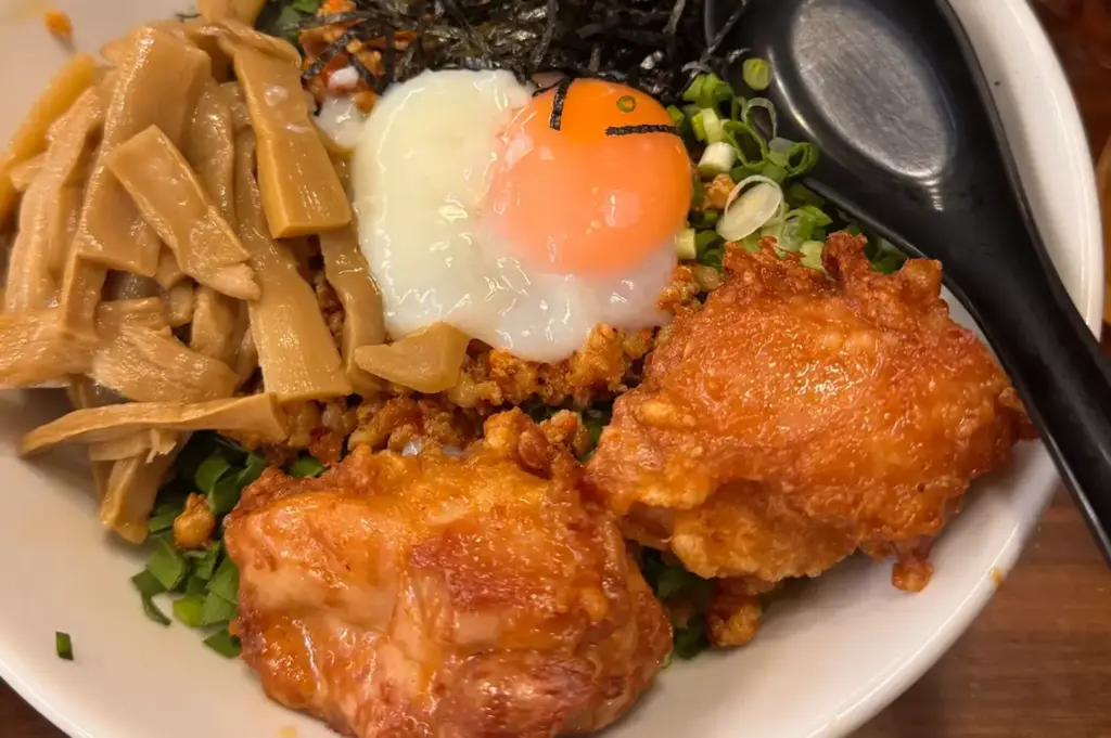 Bowl of noodles topped with fried chicken, a soft egg, bamboo shoots, scallions, seaweed, and crispy toppings.