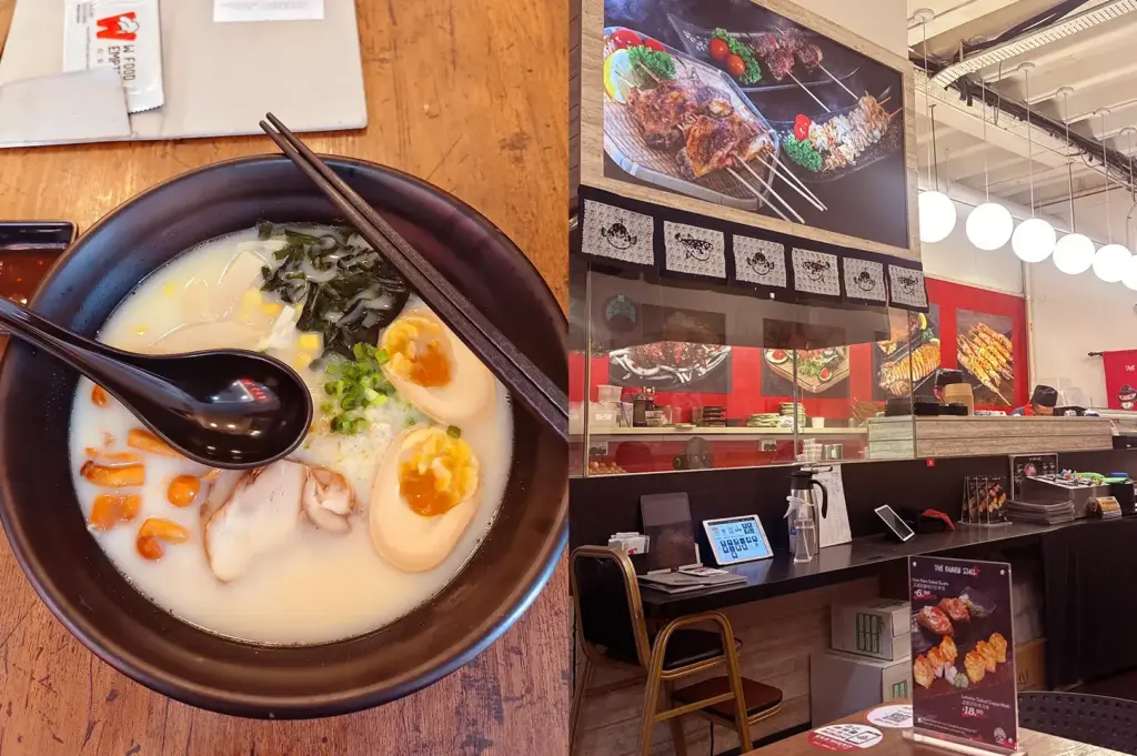 Bowl of creamy ramen topped with halved soft-boiled eggs, seaweed, spring onions, and sliced meat beside The Ramen Stall’s counter-style interior with food posters and round pendant lights.